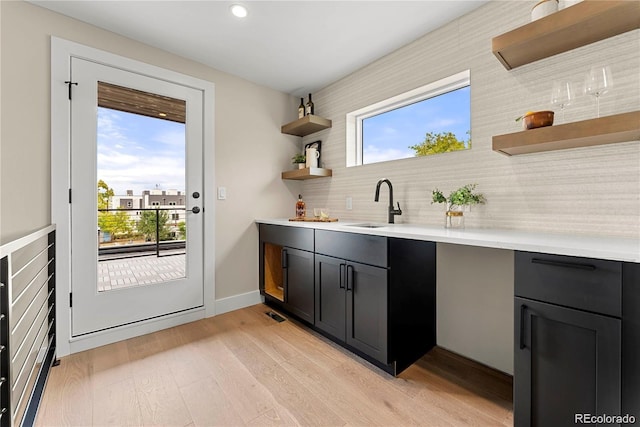 bar featuring tasteful backsplash, plenty of natural light, light wood-style flooring, and a sink