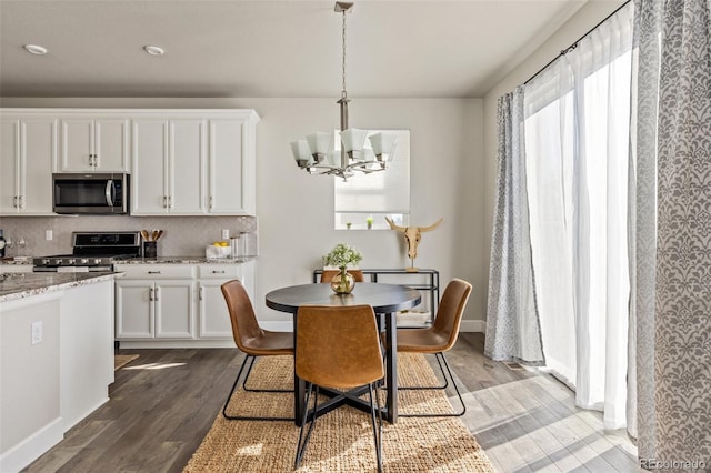 kitchen featuring appliances with stainless steel finishes, pendant lighting, white cabinets, light stone countertops, and dark wood-type flooring