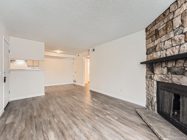 unfurnished living room with visible vents, a fireplace, baseboards, and wood finished floors