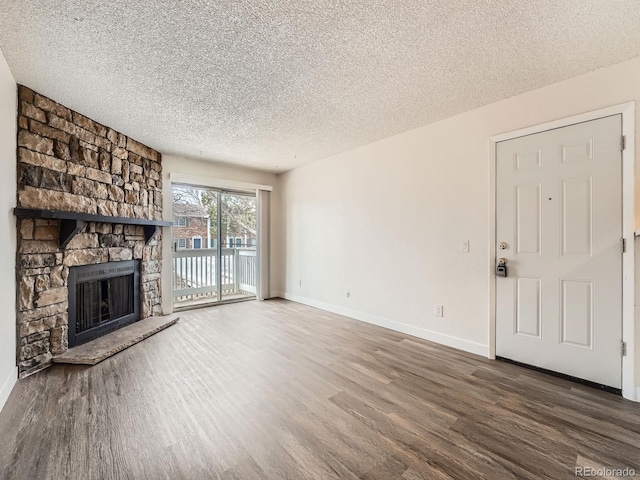 unfurnished living room with a textured ceiling, a stone fireplace, baseboards, and wood finished floors