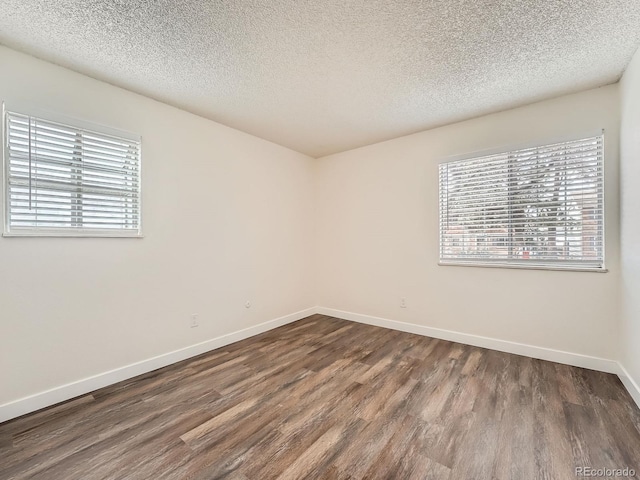 empty room featuring dark wood-style flooring, a textured ceiling, and baseboards