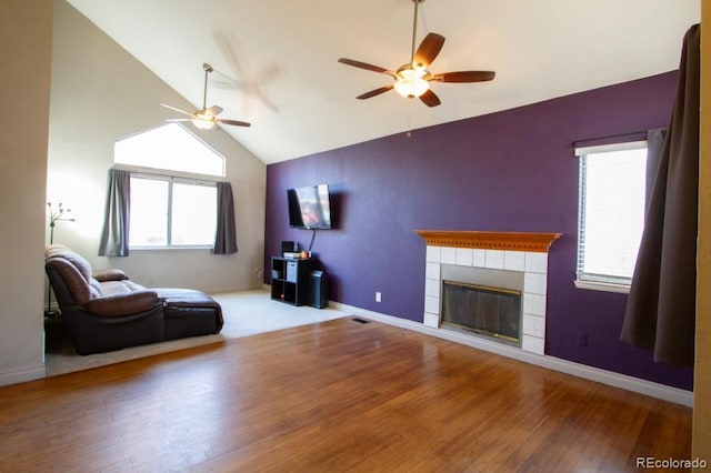 living room featuring a tile fireplace, ceiling fan, wood-type flooring, and vaulted ceiling