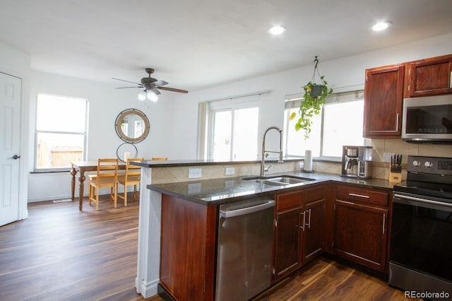 kitchen with dark wood-style flooring, stainless steel appliances, a sink, dark stone countertops, and a peninsula