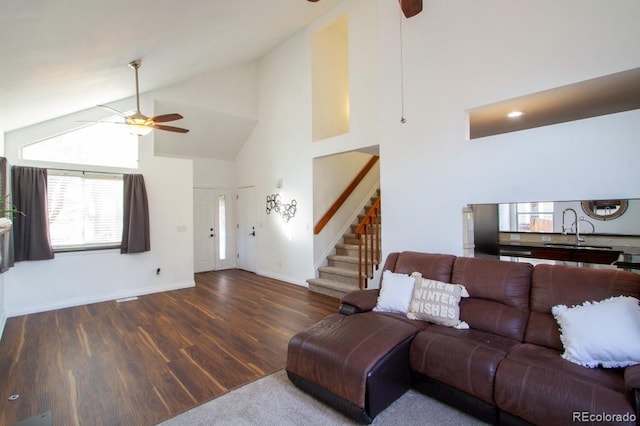 living area with high vaulted ceiling, wood finished floors, a ceiling fan, baseboards, and stairway