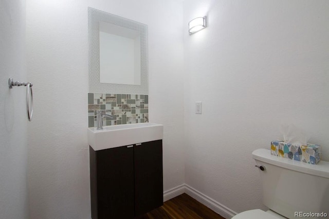 half bathroom with baseboards, vanity, toilet, and wood finished floors