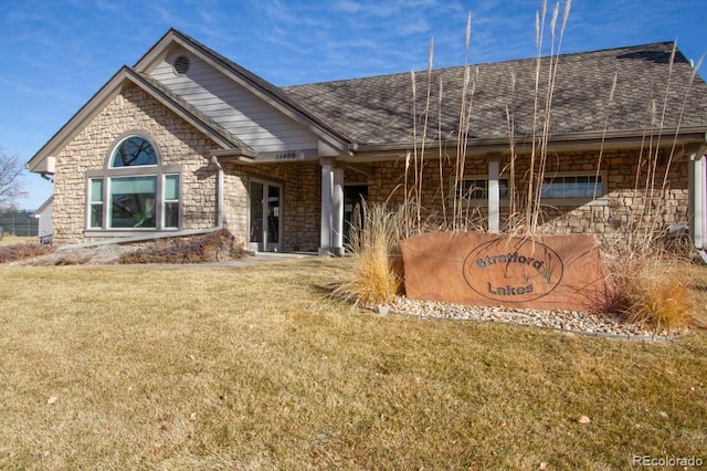 view of front of property with stone siding, a shingled roof, and a front yard