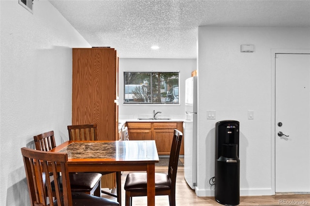 dining room featuring baseboards, a textured ceiling, visible vents, and light wood-style floors