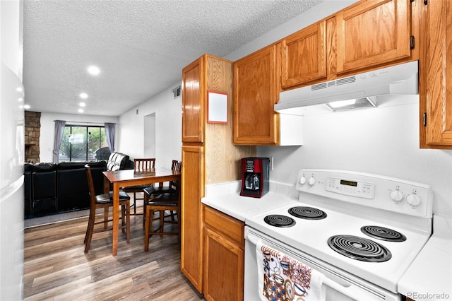kitchen with a textured ceiling, light countertops, light wood finished floors, under cabinet range hood, and electric range