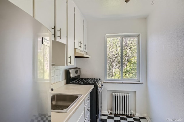 kitchen with sink, backsplash, radiator, white cabinetry, and stainless steel gas range oven