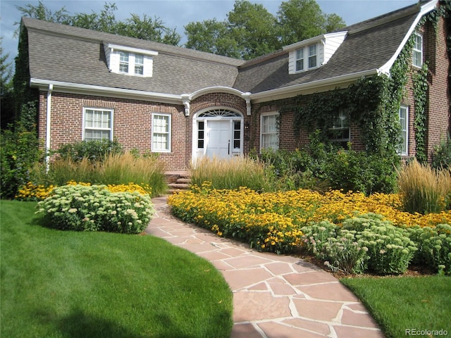 colonial inspired home with brick siding, a front lawn, and a shingled roof