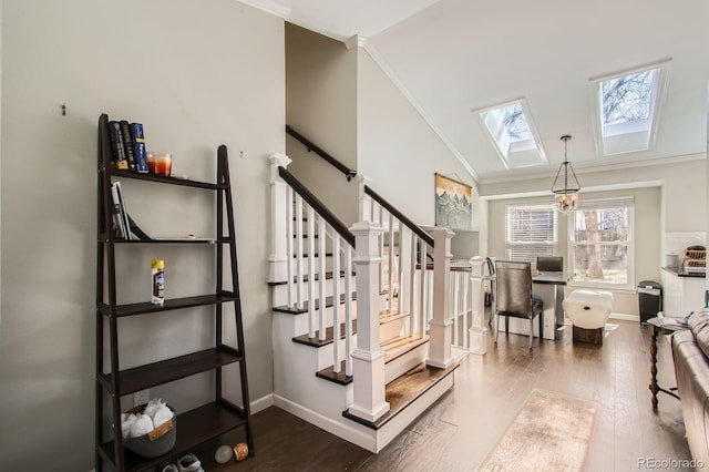 stairway featuring vaulted ceiling with skylight, crown molding, baseboards, and wood finished floors