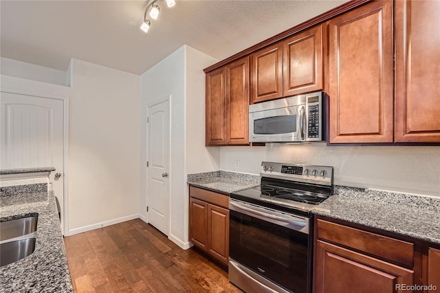 803 E 98th Ave Unit 105, Thornton, CO 80229 - kitchen with appliances with stainless steel finishes, dark wood-style flooring, dark stone countertops, brown cabinets, and baseboards