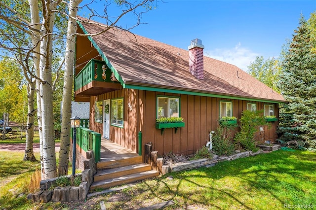 view of front of house with a balcony, a shingled roof, a chimney, and a front yard