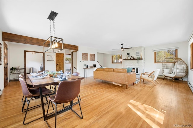 dining room featuring ceiling fan with notable chandelier, light wood-type flooring, and a brick fireplace