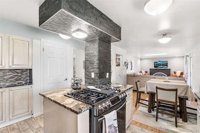 kitchen with stainless steel range with gas stovetop, backsplash, open floor plan, and light wood-type flooring