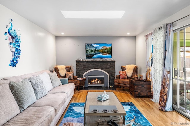 living area featuring recessed lighting, a skylight, a stone fireplace, and wood finished floors