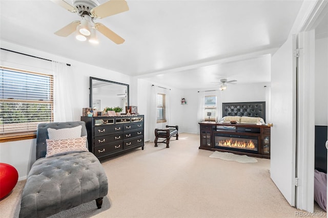 carpeted bedroom with a glass covered fireplace and ceiling fan