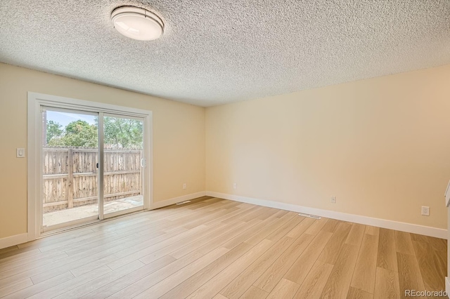 empty room featuring light wood-type flooring, a textured ceiling, baseboards, and visible vents