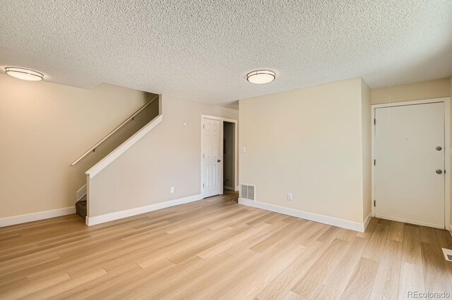 unfurnished living room with a textured ceiling, visible vents, stairway, baseboards, and light wood-style flooring