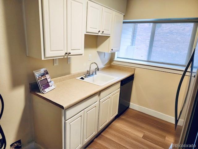 kitchen with light wood-type flooring, a sink, baseboards, black dishwasher, and white cabinetry