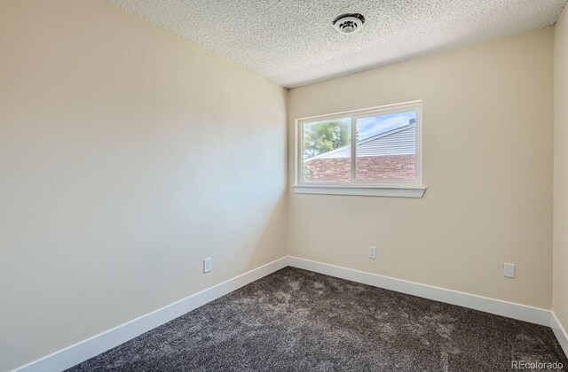 empty room featuring dark carpet, a textured ceiling, baseboards, and visible vents