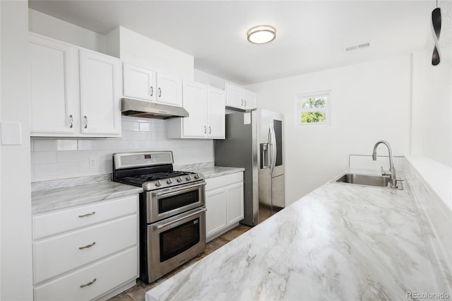1455 W Alaska Pl, Denver, CO 80223 - kitchen featuring appliances with stainless steel finishes, under cabinet range hood, light stone counters, white cabinets, and backsplash