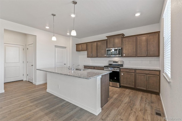 18162 Coppermallow Trl, Parker, CO 80134 - kitchen featuring appliances with stainless steel finishes, light wood-type flooring, light stone counters, decorative backsplash, and a kitchen island with sink