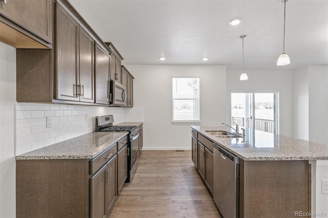 18162 Coppermallow Trl, Parker, CO 80134 - kitchen with stainless steel appliances, light wood finished floors, tasteful backsplash, a kitchen island with sink, and light stone countertops