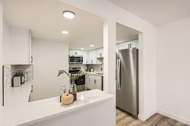 kitchen featuring stainless steel appliances, decorative backsplash, light wood-type flooring, white cabinetry, and sink