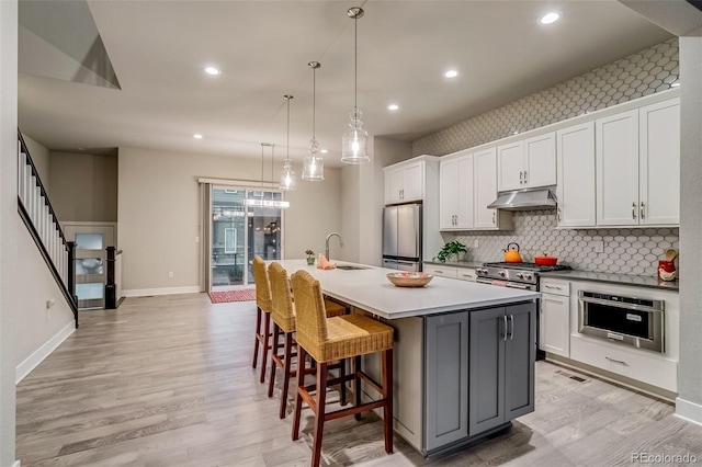 5185 Vivian St, Wheat Ridge, CO 80033 - kitchen featuring appliances with stainless steel finishes, a sink, under cabinet range hood, light wood-style floors, and a spacious island