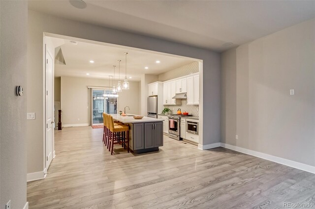 5185 Vivian St, Wheat Ridge, CO 80033 - kitchen with appliances with stainless steel finishes, under cabinet range hood, a breakfast bar area, light wood-style floors, and recessed lighting