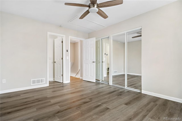 unfurnished bedroom featuring ceiling fan, dark wood-type flooring, and multiple closets