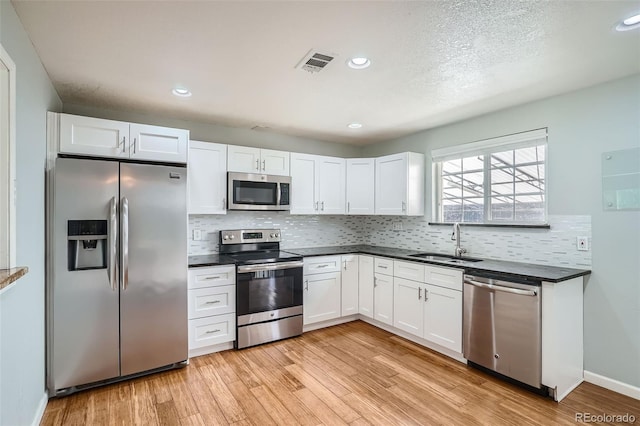 kitchen with appliances with stainless steel finishes, light wood-type flooring, tasteful backsplash, sink, and white cabinetry