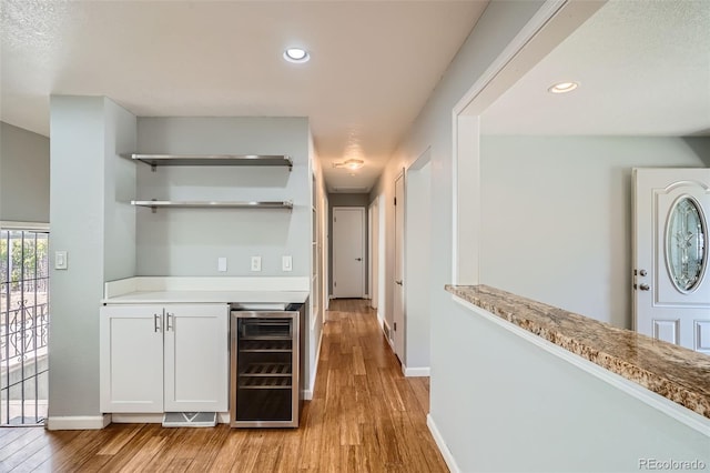 bar with light wood-type flooring, white cabinetry, and beverage cooler