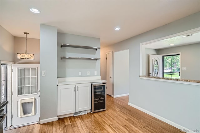 kitchen with white cabinetry, hanging light fixtures, wine cooler, and light hardwood / wood-style flooring