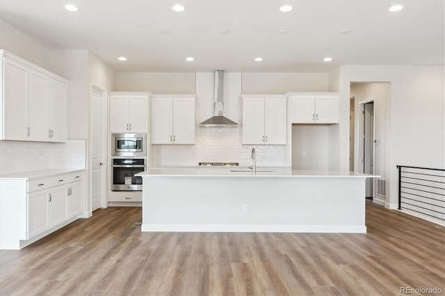 4978 Hickory Oaks St, Castle Rock, CO 80104 - kitchen featuring wall chimney exhaust hood, appliances with stainless steel finishes, a sink, a center island with sink, and white cabinetry