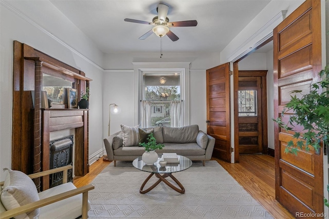 living area featuring a ceiling fan, light wood-style flooring, and a fireplace