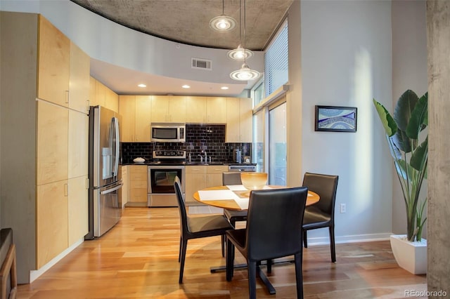 kitchen featuring dark countertops, decorative backsplash, appliances with stainless steel finishes, light wood-style floors, and light brown cabinets