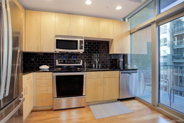 kitchen with appliances with stainless steel finishes, backsplash, light wood-type flooring, and light brown cabinets