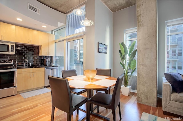 dining space with a high ceiling, visible vents, and light wood finished floors