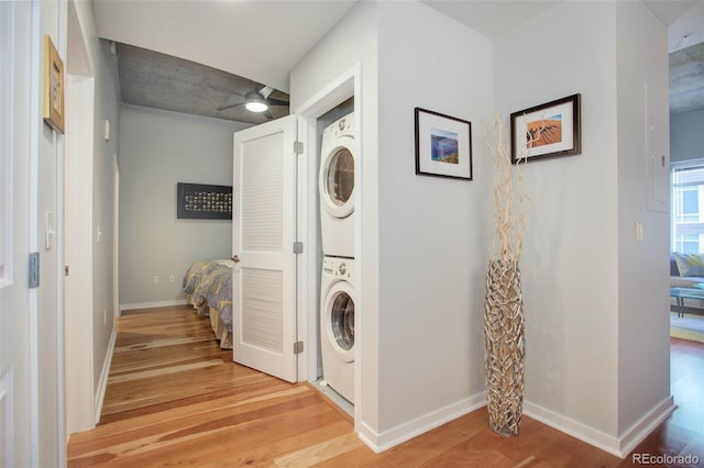 laundry room with laundry area, a ceiling fan, baseboards, light wood-type flooring, and stacked washing maching and dryer