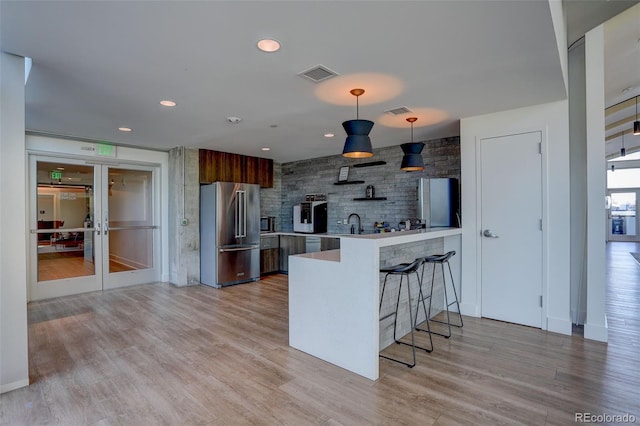 kitchen featuring a peninsula, high end refrigerator, visible vents, light wood-style floors, and a kitchen bar