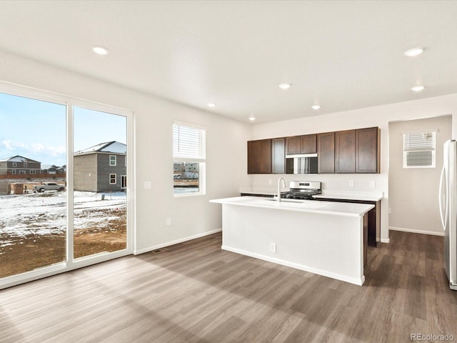 kitchen with dark wood-type flooring, freestanding refrigerator, a center island with sink, and dark brown cabinets