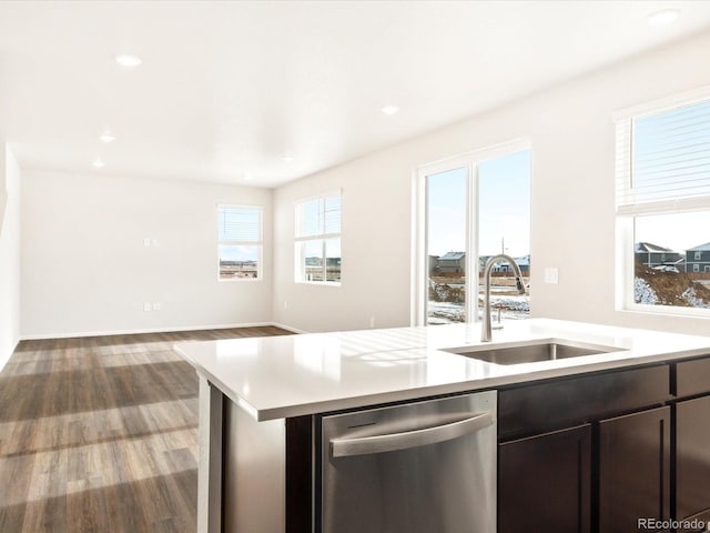 kitchen featuring a center island with sink, wood finished floors, light countertops, stainless steel dishwasher, and a sink