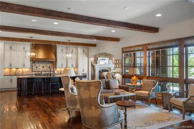 living area featuring dark wood-type flooring, a lit fireplace, beamed ceiling, a chandelier, and recessed lighting