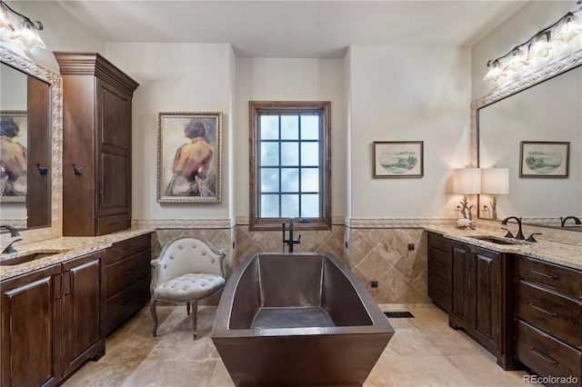 full bath featuring tile walls, a soaking tub, two vanities, a wainscoted wall, and tile patterned floors