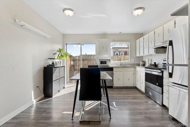 kitchen with under cabinet range hood, dark wood-style floors, white cabinetry, appliances with stainless steel finishes, and baseboards