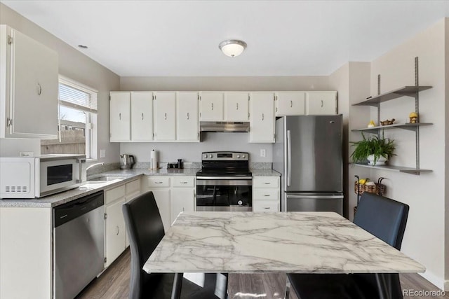 kitchen with under cabinet range hood, a sink, appliances with stainless steel finishes, white cabinets, and dark wood-style flooring