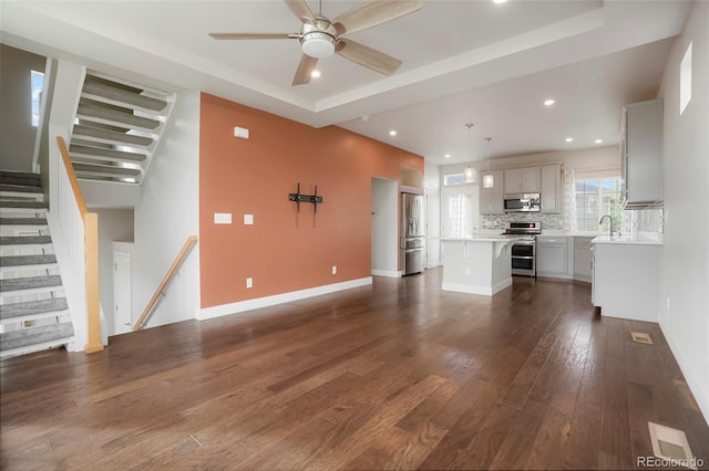 unfurnished living room featuring a tray ceiling, dark hardwood / wood-style flooring, ceiling fan, and sink