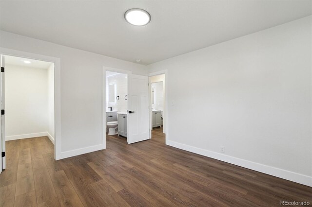 2840 Cottonwood Dr, Denver, CO 80221 - unfurnished bedroom with connected bathroom, dark wood-type flooring, baseboards, and a walk in closet